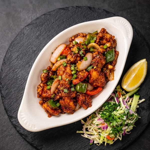 Saucy chicken with bell peppers and onions, garnished with scallions, served with a side salad and lemon.