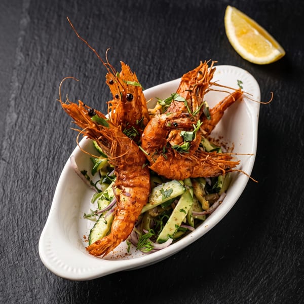 Crispy whole shrimp on a fresh cucumber and red onion salad, with herbs and a lemon slice.